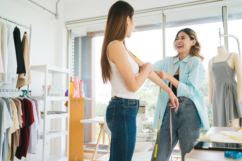 Asian woman tailor measures customers' bodies to make new clothes. Attractive female fashion designer dressmaker working and designing new fashion collections for customers in atelier tailor workshop.